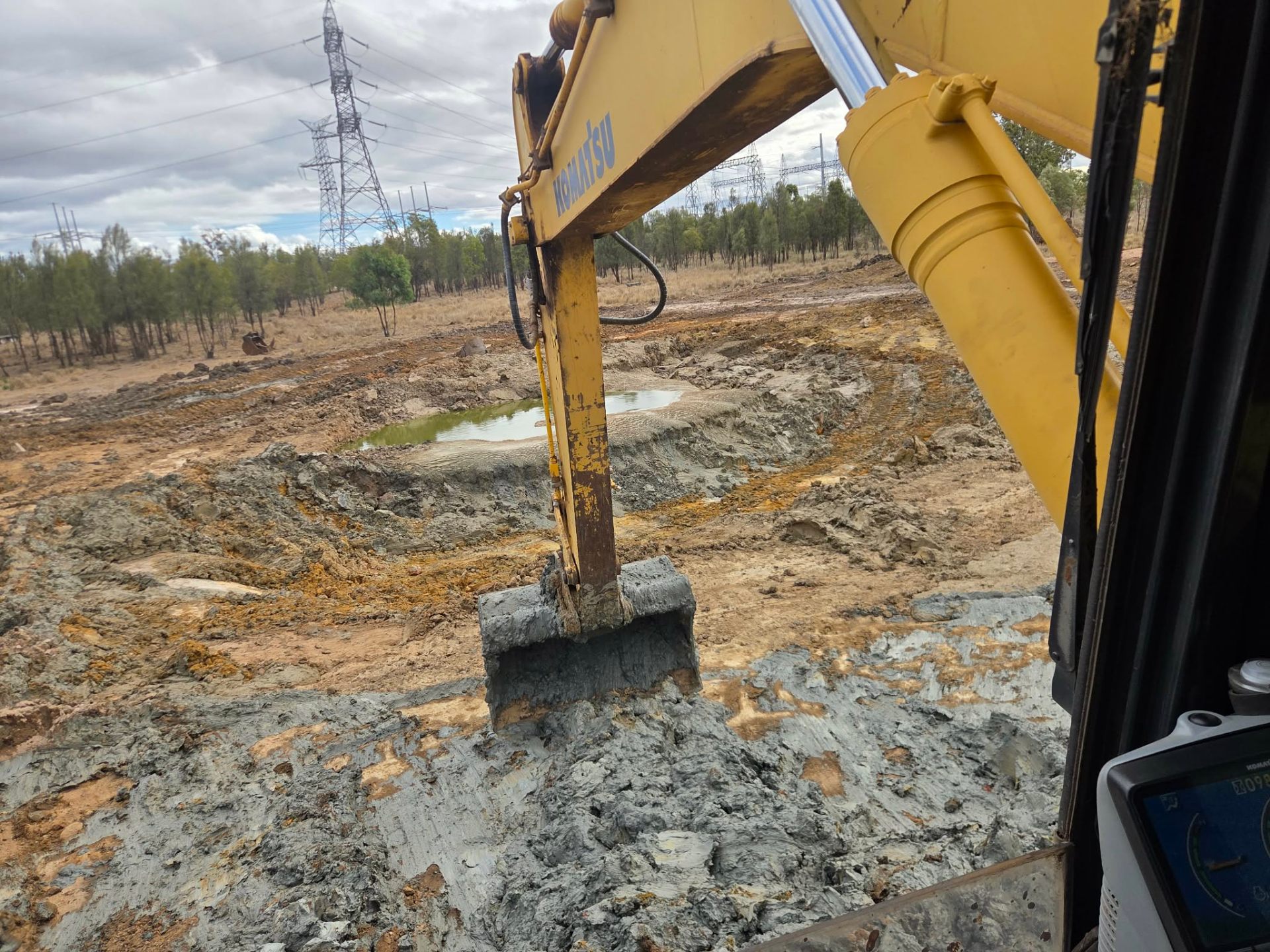 View from inside an excavator cab digging into wet clay on a new dam build