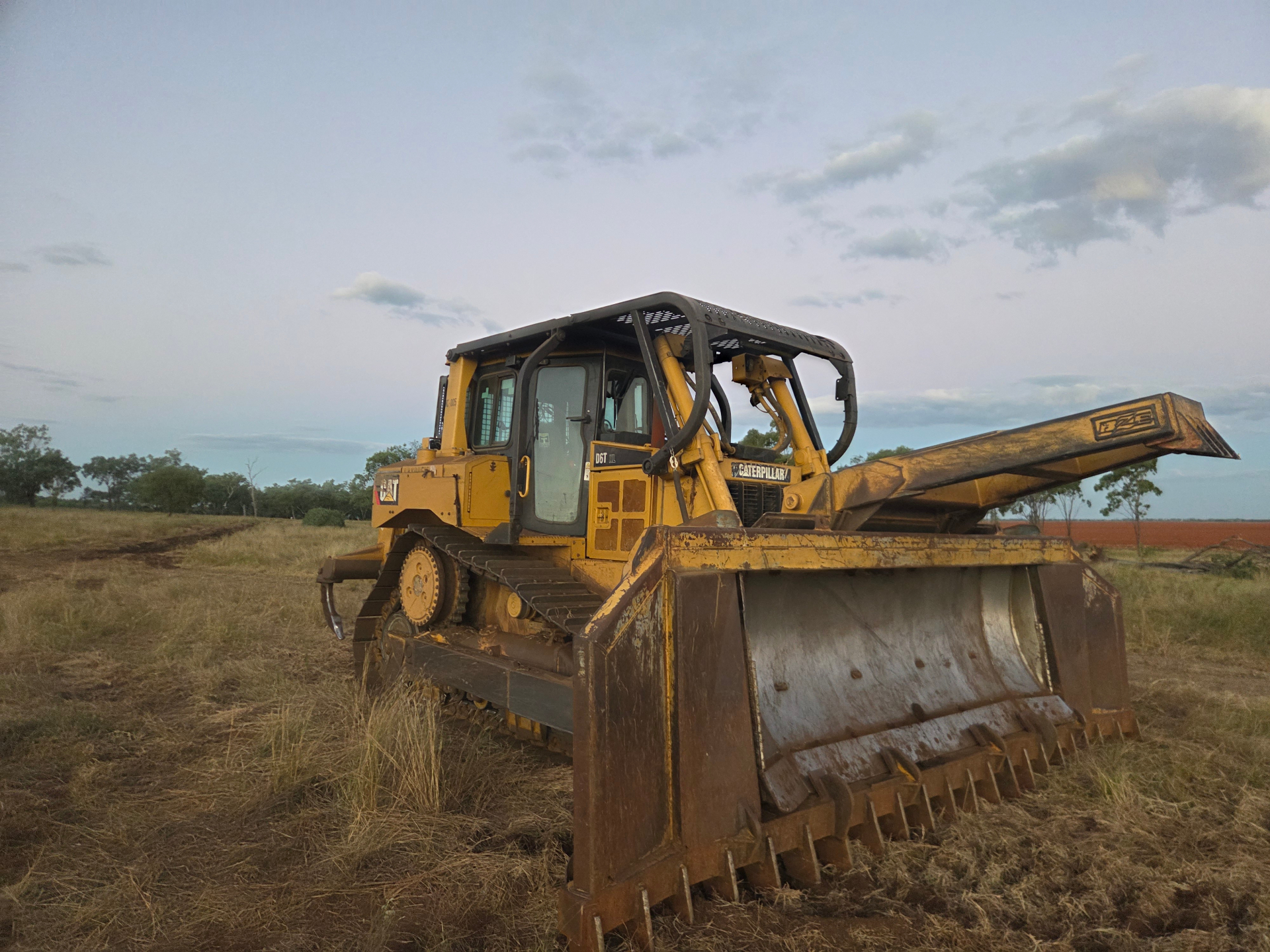 CAT D6T dozer with stick rake on a rural property at dusk