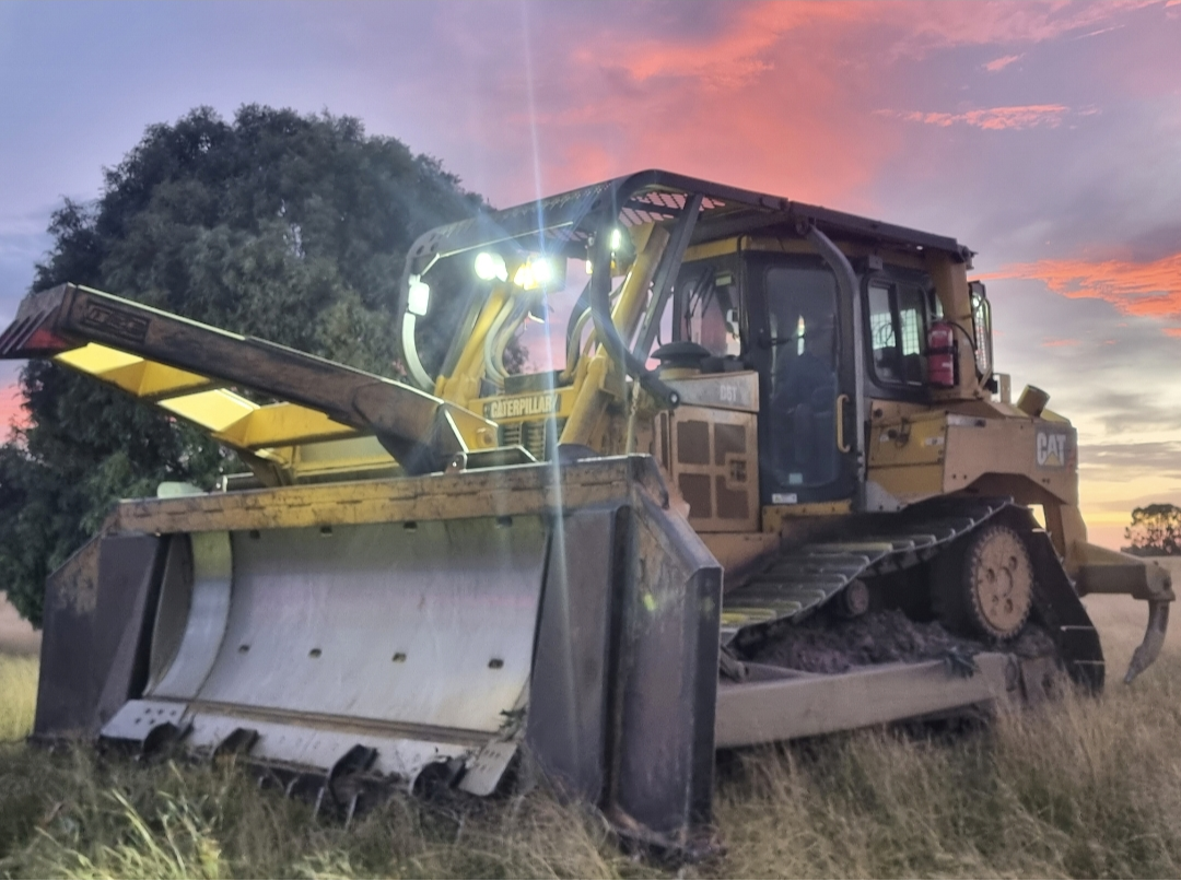 CAT D6T dozer with stick rake and blade silhouetted against a pink sunset on a Darling Downs paddock