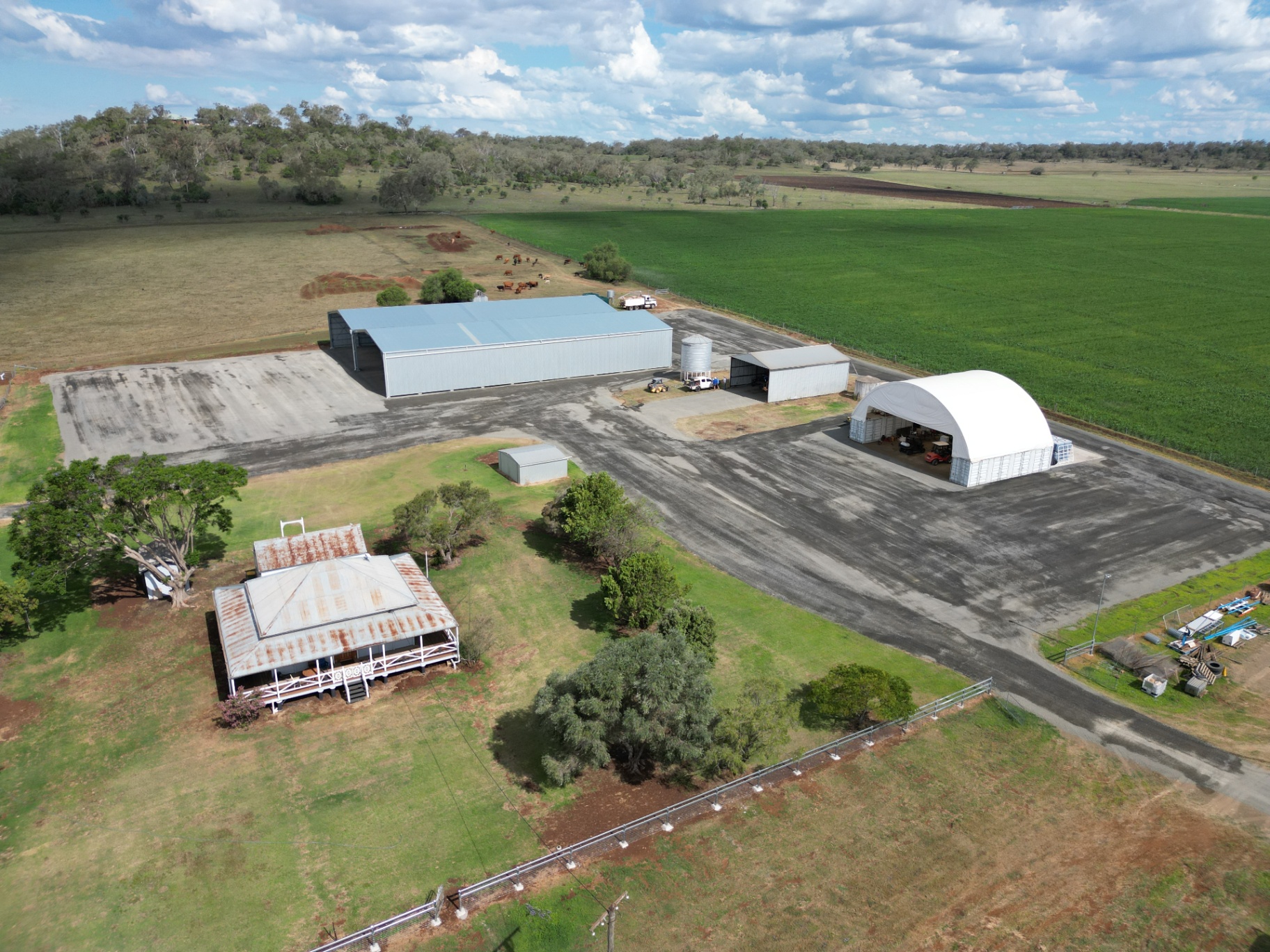 Aerial view of a farm complex with sheds, dome shelter and a large compacted hardstand area showing gravel colour variation as it cures
