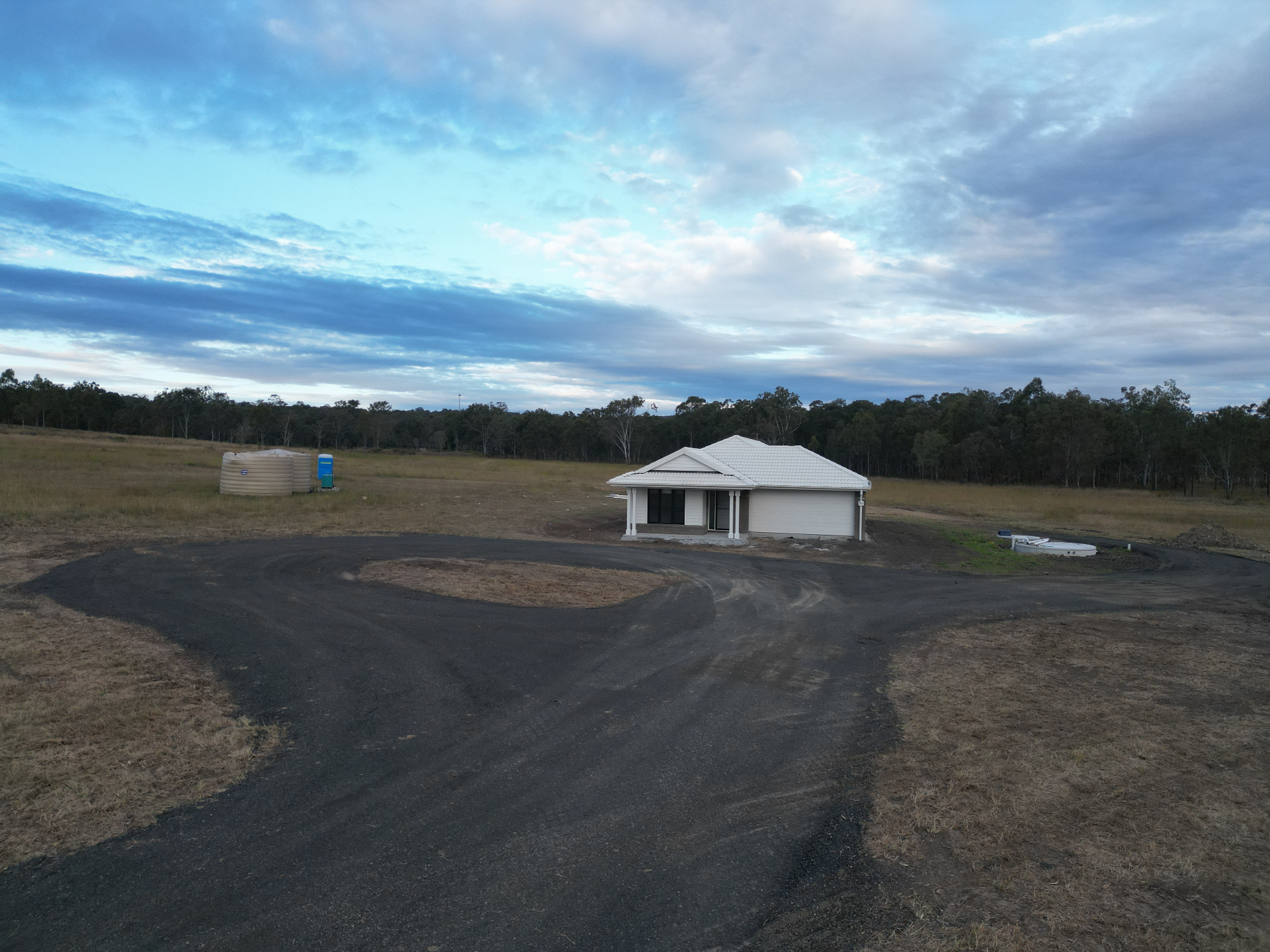 Aerial view of a finished lifestyle block with new home, sealed driveway and tank stand