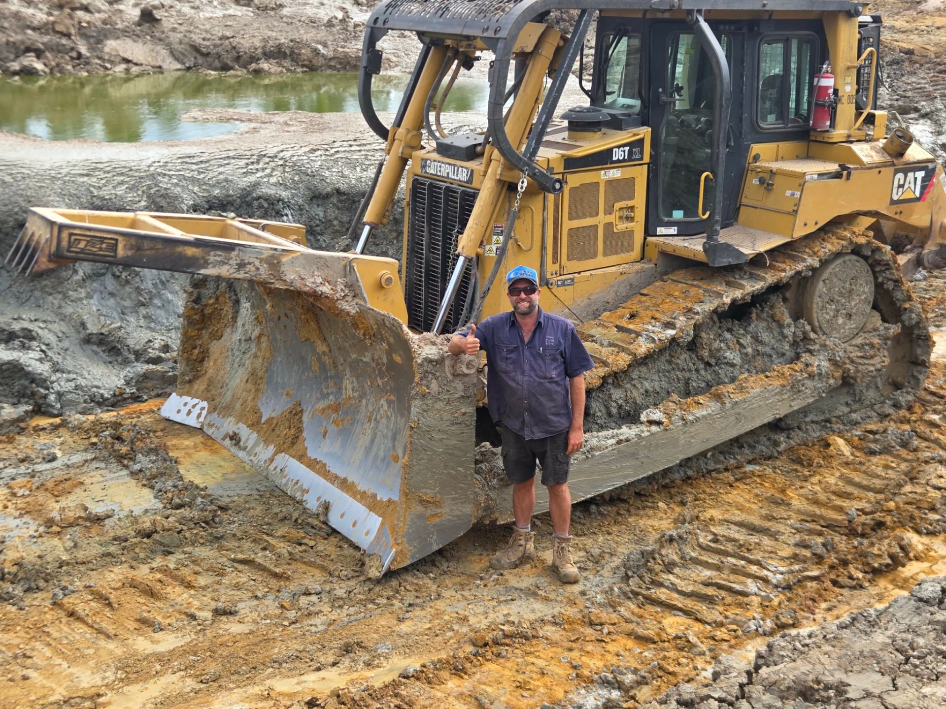 Tyrone standing by the blade of a CAT D6T dozer with cap on